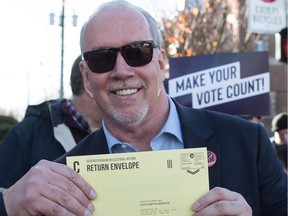 Premier John Horgan holds a voter's electoral reform referendum ballot while walking to a mailbox after a rally in Vancouver