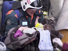 This photo provided by the Russian Emergency Situations Ministry taken from tv footage shows a Emergency Situations employee carrying a baby at the scene of a collapsed section of an apartment building, in Magnitigorsk, Russia, Tuesday, Jan. 1, 2019. (Russian Ministry for Emergency Situations photo via AP)