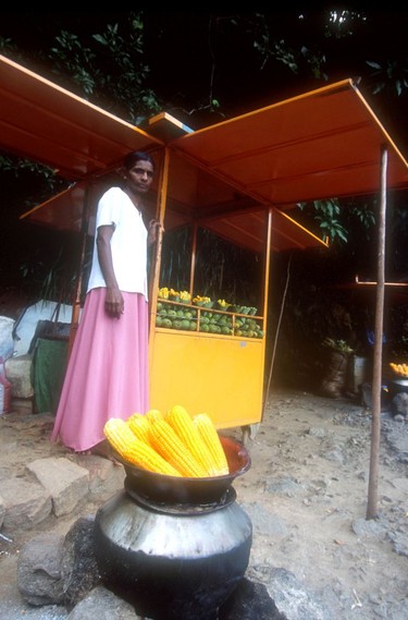 A Sri Lankan woman sells corn and mango slices from her stall.