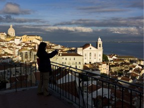 A tourist takes photos from a viewpoint overlooking Lisbon's Alfama neighborhood and the Tagus river. The Alfama quarter is distinguished by its narrow, cobbled streets on the hillside below Lisbon castle, where archaeologists have found traces of occupation dating from the seventh century B.C.