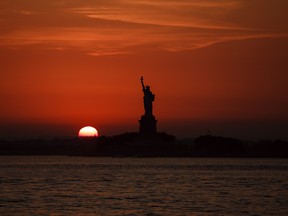 In this July 1, 2018, file photo, the sun sets behind the Statue of Liberty in New York.