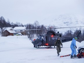 A military helicopter and rescue workers arrive to take part in the search for four missing skiers in the nearby mountain in Tamokdalen, Northern Norway, Friday, Jan. 4, 2019. Norwegian officials say four people from Sweden and Finland are missing after an avalanche but strong winds, heavy snowfall and poor visibility are hampering rescue efforts.