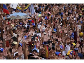 Anti-government protesters hold their hands up during the symbolic swearing-in of Juan Guaido, head of the opposition-run congress, who declared himself interim president of Venezuela, during a rally demanding President Nicolas Maduro's resignation in Caracas, Venezuela, Wednesday, Jan. 23, 2019.