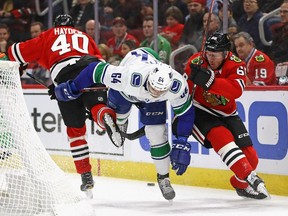 Tyler Motte of the Vancouver Canucks loses his balance while battling for the puck between John Hayden, left, and Slater Koekkoek of the Chicago Blackhawks at the United Center on Thursday in Chicago, Ill.