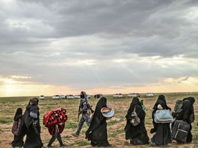 Women, covered in their abaya and niqab, clutch their children close and lug their remaining belonging behind, monitored by SDF forces.