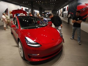 In this July 6, 2018, file photo prospective customers confer with sales associates as a Model 3 sits on display in a Tesla showroom in the Cherry Creek Mall in Denver.