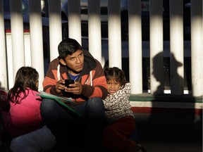 A migrant who did not give his name looks on with his children as they wait to hear if their number is called to apply for asylum in the United States, at the border in Tijuana, Mexico, on Jan. 25, 2019.