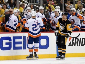Sidney Crosby (right) of the Pittsburgh Penguins skates off the ice as Anders Lee of the New York Islanders celebrates with teammates on the bench after scoring an empty-net goal in the third period of Game 3 of their NHL Eastern Conference first-round series at PPG PAINTS Arena in Pittsburgh on Sunday, April 14, 2019.
