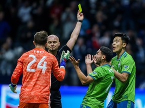 Referee Robert Sibiga shows a yellow card against Seattle Sounders' Kim Kee-hee (20) near Seattle Sounders goalkeeper Stefan Frei (24) and Cristian Roldan (7) during the second half MLS soccer action in Vancouver, B.C., on Saturday March 30, 2019.