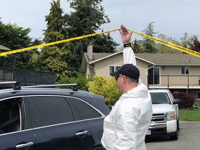 Forensic identification officer lifts police tape for neighbour outside Brentwood Bay home where one person was killed and two seriously injured Saturday morning.