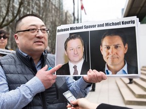 In this file photo taken on March 6, 2019, Louis Huang of Vancouver Freedom and Democracy for China holds photos of Canadians Michael Spavor and Michael Kovrig, who are being detained by China, in Vancouver.