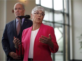 B.C. Premier John Horgan looks on as Finance Minister Carole James answers a question during a media scrum in Nanaimo, B.C., on Wednesday, August 22, 2018. British Columbia has introduced legislation for Canada's first public registry of property owners to prevent hidden ownership in an effort to stop tax evasion and money laundering. Photo: Chad Hipolito/CP