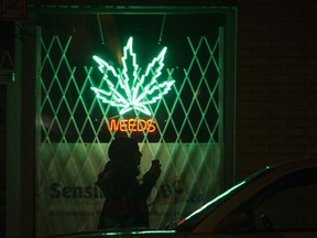 A pedestrian walks  past the Weeds neon sign on Burrard Street, Vancouver, in 2014.