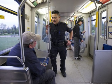 Transit Police Const. Darren Chua talks with a customer as he rides a SkyTrain between the Surrey Central and Gateway Skytrain stations.
