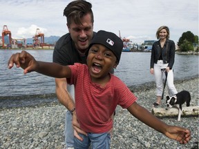 Kim and Clark Moran and their adopted son Ayo play along the beach at Crab park Vancouver, July 12 2019. The family dog is Zola. Photo: Gerry Kahrmann/Postmedia