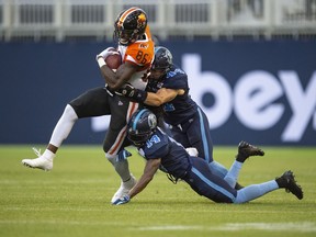 B.C. Lions wide receiver Jevon Cottoy hangs on to the ball while being tackled by Toronto Argonauts linebacker Ian Wild and teammate Abdul Kanneh, right, during CFL action in Toronto on Saturday.