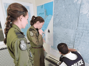 Members of a Royal Canadian Air Force Hercules flight crew looks over a map with an RCMP officer during a manhunt for Kam McLeod and Bryer Schmegelsky.