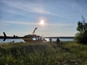Officers look through a remote lake area alongside a landed helicopter in the Gillam, Man., area in July 28, 2019, police image published to social media.