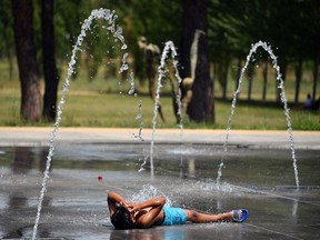 A boy lies on the pavement as he cools off under water jets at a fountain in Montpellier on June 27, 2019, southern France, during a heat wave. Europeans braced on June 27, 2019 for the expected peak of a sweltering heatwave that has sent temperatures soaring above 40 degrees Celsius.