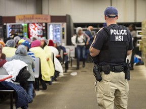This image released by the U.S. Immigration and Customs Enforcement (ICE) shows a Homeland Security Investigations (HSI) officer guarding suspected illegal aliens on August 7, 2019.