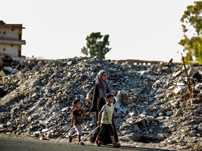 A woman and two children walk past debris in the northern Syrian city of Raqa, the former Syrian capital of the Islamic State, on Aug. 21. Othman Hamdan has been ordered deported from Canada after online praise for lone-wolf attacks carried out by the terrorist group.