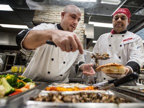 Longo's food service manager Marco DiVincenzo, left, and co-worker VJ, right, serve food for a customer at the grocery store’s kitchen in north Toronto.
