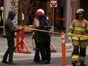 Friends hug a one of two maintenance workers, in white helmet, caught in a wind storm who was rescued by Edmonton Fire Rescue Service firefighters in Edmonton, on Friday, Oct. 25, 2019. Photo by Ian Kucerak/Postmedia
