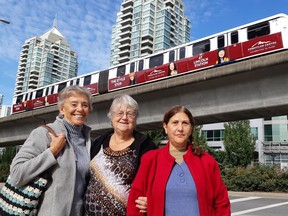 Three women who are members of a seniors committee pose in front of a SkyTrain.