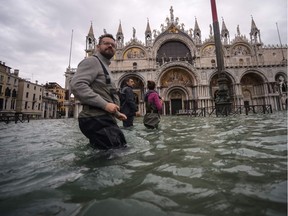 TOPSHOT - A general view shows people walking across the flooded St. Mark's Square, by St. Mark's Basilica on November 15, 2019 in Venice, two days after the city suffered its highest tide in 50 years. - Flood-hit Venice was bracing for another exceptional high tide on November 15, as Italy declared a state of emergency for the UNESCO city where perilous deluges have caused millions of euros worth of damage. (Photo by Filippo MONTEFORTE / AFP)