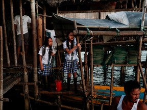 Sisters Cindy (left), age 14, and 16-year-old Danica Martinez prepare to board a boat to travel to school with their father Domingo (front right) in the submerged coastal village Sitio Pariahan, Bulakan, Bulacan, north of Manila, Philippines, on Nov. 25, 2019.