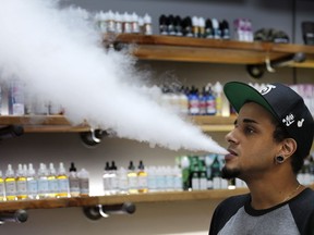 In this Tuesday, Sept. 3, 2019, photo, Andrew Teasley, a salesman at Good Guys Vape Shop, exhales vapor while using an e-cigarette in Biddeford, Maine. Health Canada is proposing to ban advertising of vaping products in spaces where young people can see them in a bid to rein in the rise of underage e-cigarette use.
