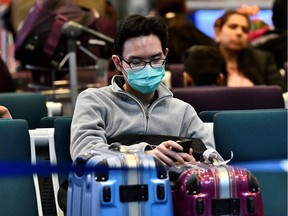 A traveller wearing a mask, sits at Vancouver International Airport (YVR) as Canada's Public Health Agency added a screening question for visitors and began displaying messages in several airports urging travellers to report flu-like symptoms in efforts to prevent any introduction of coronavirus, in Richmond, British Columbia, Canada January 24, 2020.  REUTERS/Jennifer Gauthier