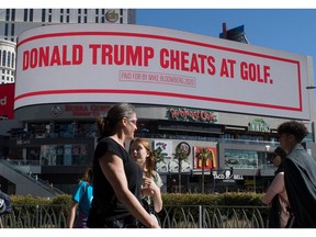 People walk past a billboard paid for by Democratic presidential hopeful Mike Bloomberg, that is attacking President Trump and is displayed on the iconic Las Vegas Strip, in Nevada, on February 21, 2020.