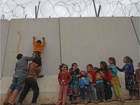 TOPSHOT - Displaced Syrian children try to climb over the Turkish border wall at an informal camp in Kafr Lusin village in Syria's northwestern province of Idlib, on February 21, 2020. - Six months ago, the family fled deadly fighting in Idlib province of northwest Syria, seeking shelter near the border village of Kafr Lusin, where dozens of families live in an informal camp for the displaced. Turkey, which already hosts the world's largest number of Syrian refugees with around 3.6 million people, has placed barbed wire and watchtowers along the wall to prevent any more crossings. (Photo by AAREF WATAD / AFP)