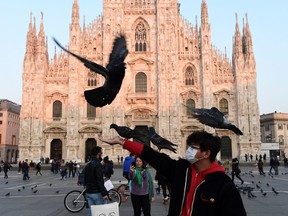 A man wearing a protective face mask plays with pigeons in the Piazza del Duomo in central Milan, on Feb. 24, 2020.