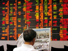 A Thai investor reads a newspaper in front of an electronic board displaying live market data at a stock broker's office in Bangkok, Thailand.