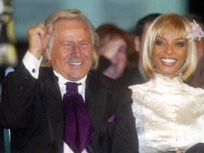 Fashion mogul Peter Nygard, clad in a rich eggplant tie and slick black suit, raises a fist in triumph while sitting front-and-centre at his show with Yves-Lauren.