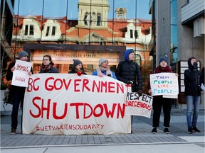 Protestors stand outside the Business Development Bank of Canada in Victoria, with City Hall reflected in the windows.