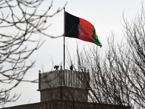 An Afghan security personnel keeps watch on a tower as the Afghan national flag flutters.