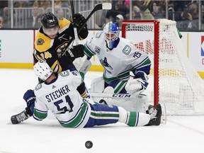 Vancouver Canucks' netminder Jacob Markstrom keeps an eye on a loose puck as defenceman Troy Stecher falls into his crease in front of Boston Bruins' Jake DeBrusk.