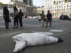 People walk past a homeless person sleeping on the street in downtown Vancouver on Tuesday, March 17, 2020.