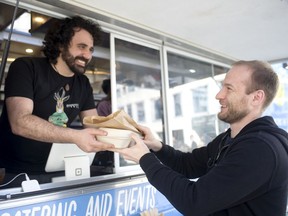 Itamar Shani, owner of the I Love Chickpea food truck, hands lunch to customer David Laszuk near the corner of Cordova and Howe streets in Vancouver.