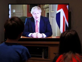 Two children watch in Hertford, Britain, as British Prime Minister Boris Johnson delivers a televised address on the spread of COVID-19 coronavirus on March 23, 2020.