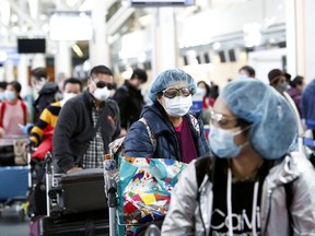 People wearing face masks and goggles wait to check in for an international flight at the Vancouver International Airport.