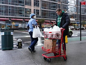 A man with a cart of groceries and a woman with a protective mask and groceries pass on the street during the coronavirus pandemic on April 13, 2020 in New York City.