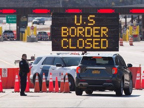 In this file photo U.S. Customs officers speaks with people in a car beside a sign saying that the U.S. border is closed at the US/Canada border in Lansdowne, Ont., on March 22, 2020. (LARS HAGBERG/AFP via Getty Images)