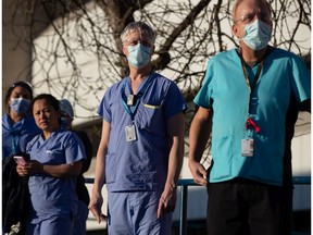 Health care workers in New Westminster watch a Thursday procession of first responders drive past Royal Columbian Hospital with lights and sirens activated in a show of support for staff treating those affected by COVID-19.