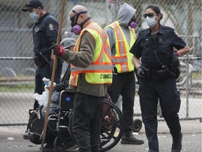 Vancouver police keep watch while City of Vancouver workers clear debris from East Hastings Street in Vancouver's Downtown Eastside on April 17.