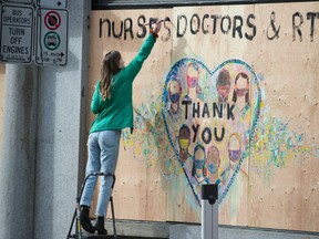 A woman paints a thank you message to nurses and doctors on a boarded up shop in downtown Vancouver on Wednesday, April 1.