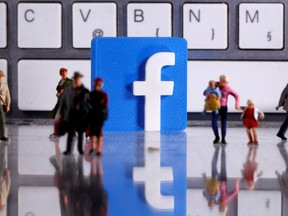 A 3D printed Facebook logo is placed between small toy people figures in front of a keyboard in this illustration taken April 12, 2020.